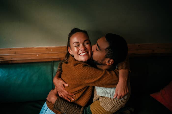 A smiling woman and a man are hugging on a couch, sharing an intimate and joyful moment
