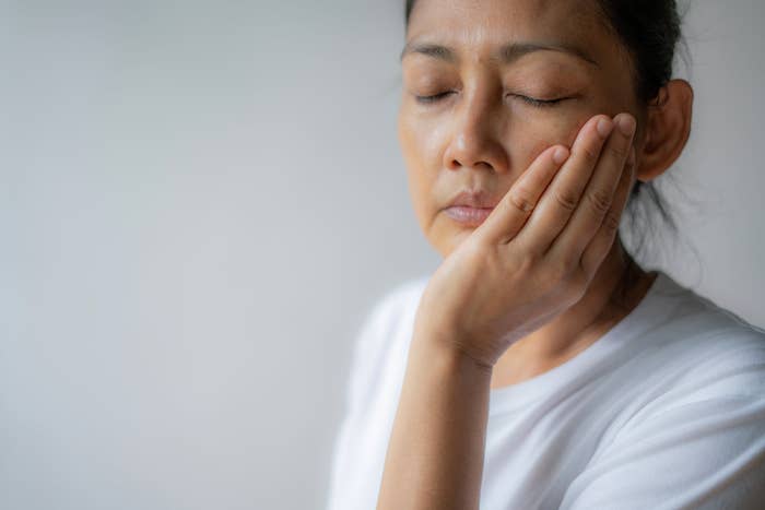 A person with closed eyes holds their hand to their cheek, appearing to be in discomfort or deep thought
