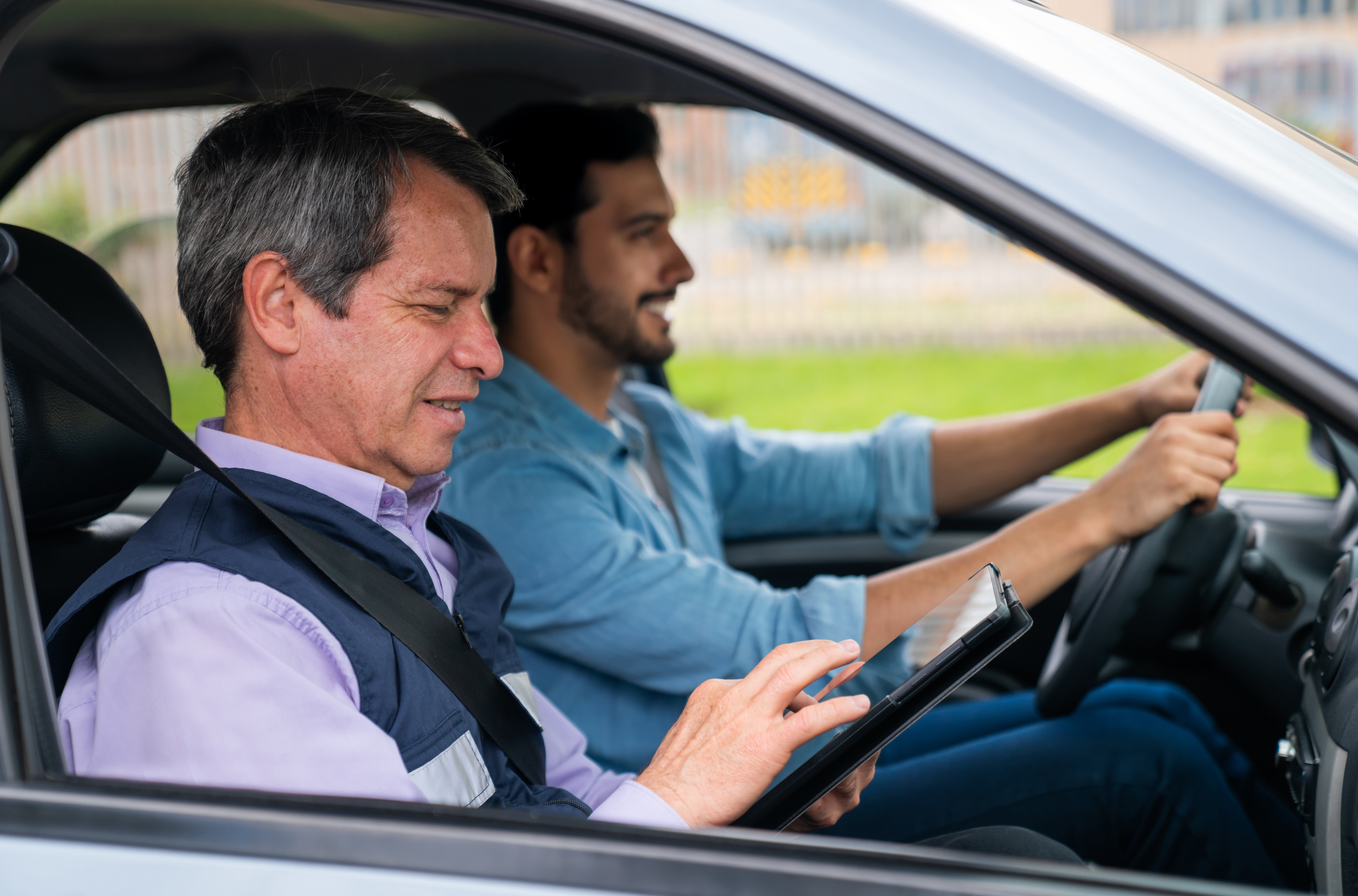 Two men in a car, one driving and the other using a tablet
