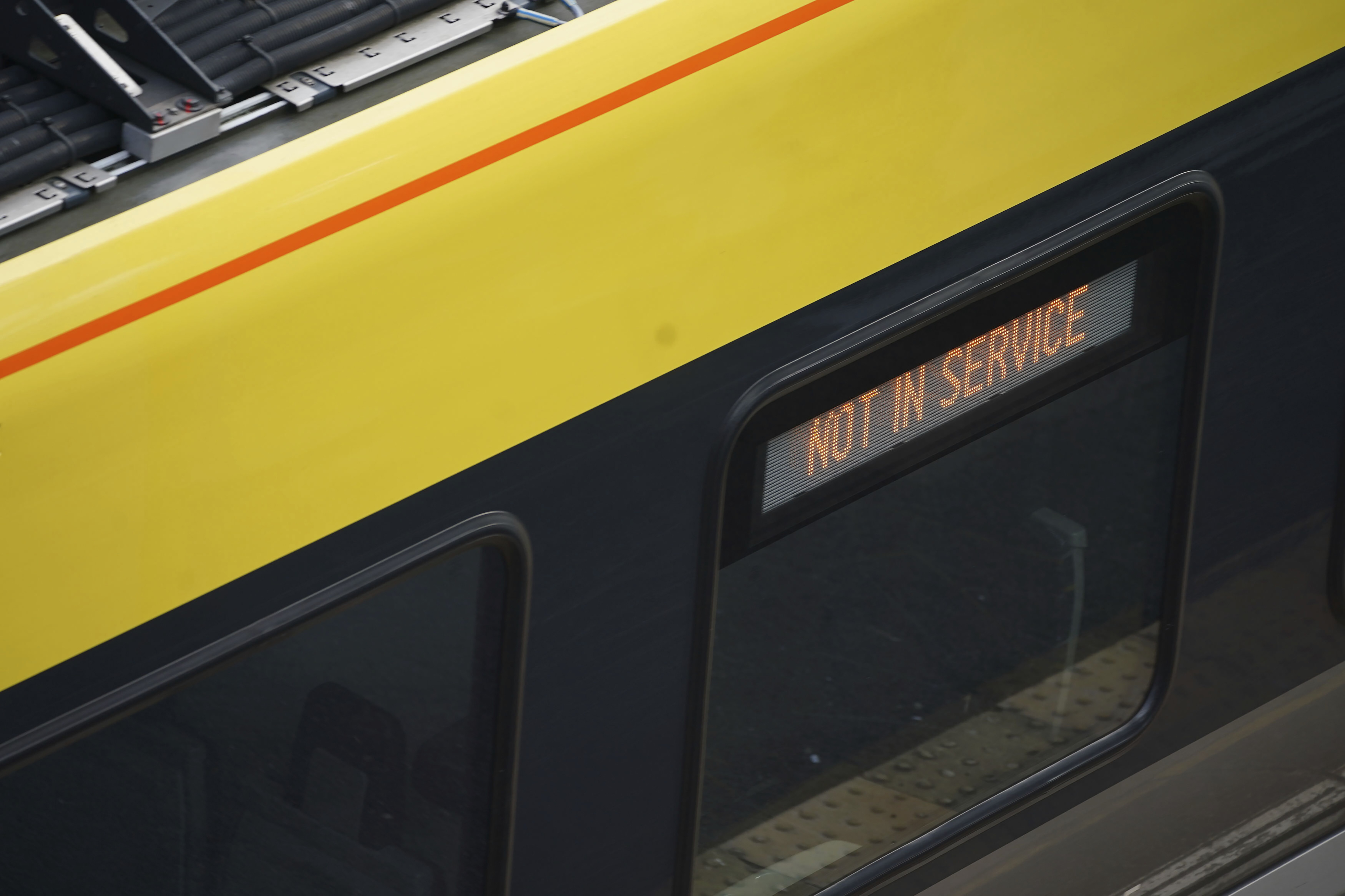 A train with a digital display reading "NOT IN SERVICE" at a station platform