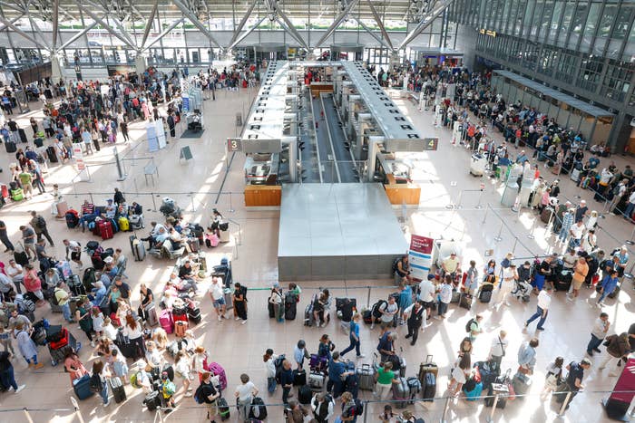 A large crowd of travelers waits in multiple lines at an airport check-in area, with numerous suitcases and bags, under a high-ceiling terminal