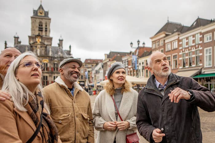 Group of five adults, dressed warmly, stand together in a historic European town square, looking at an unseen point of interest