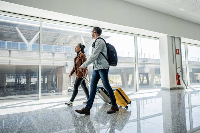 Two travelers walking through an airport terminal with their luggage