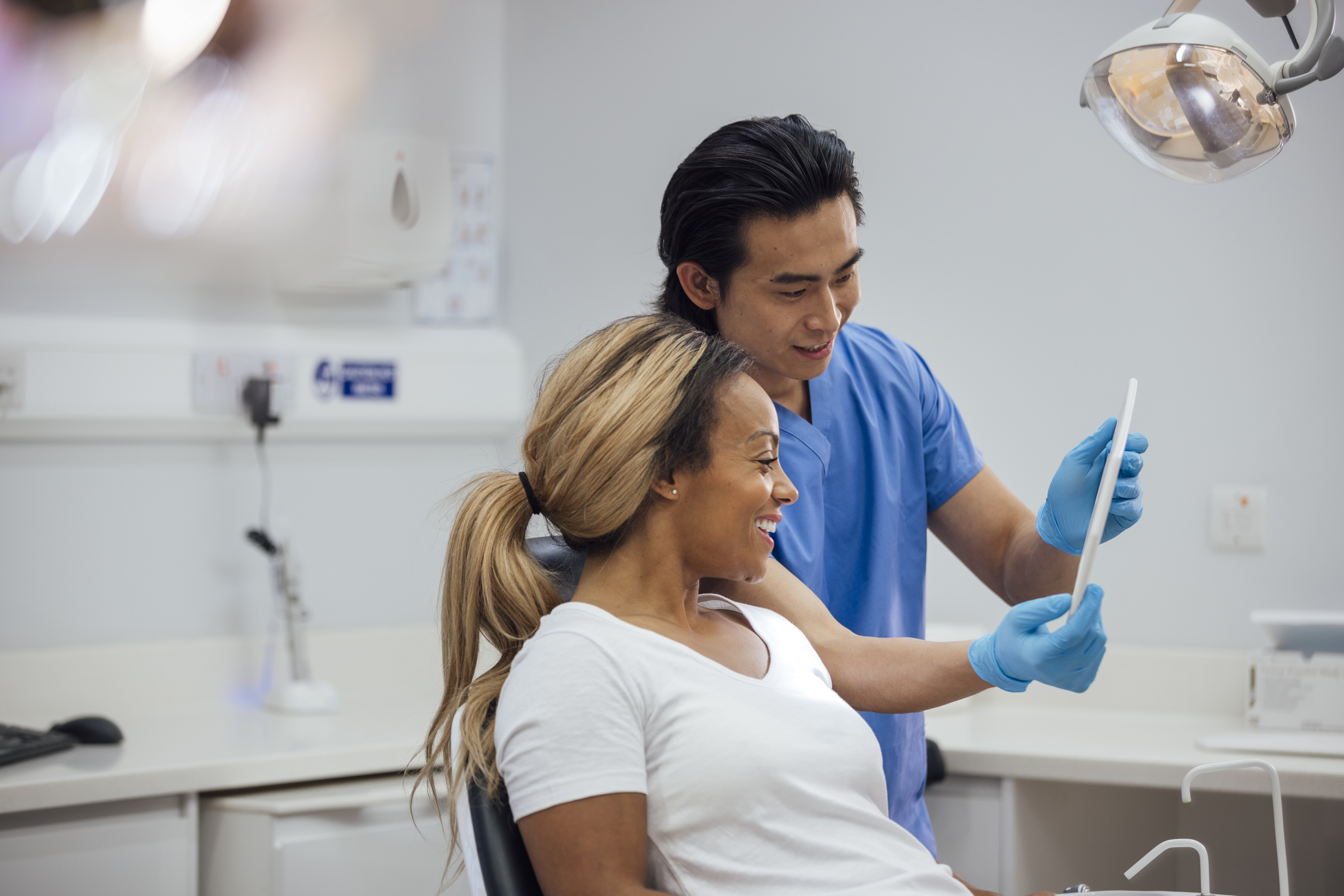 A dental professional shows a patient, who is smiling, something on a tablet. They are in a modern dental office. Names not known