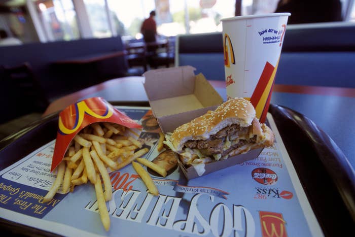 Fast food tray with a McDonald&#x27;s burger, fries, and drink inside a restaurant. Tray liner shows advertising material