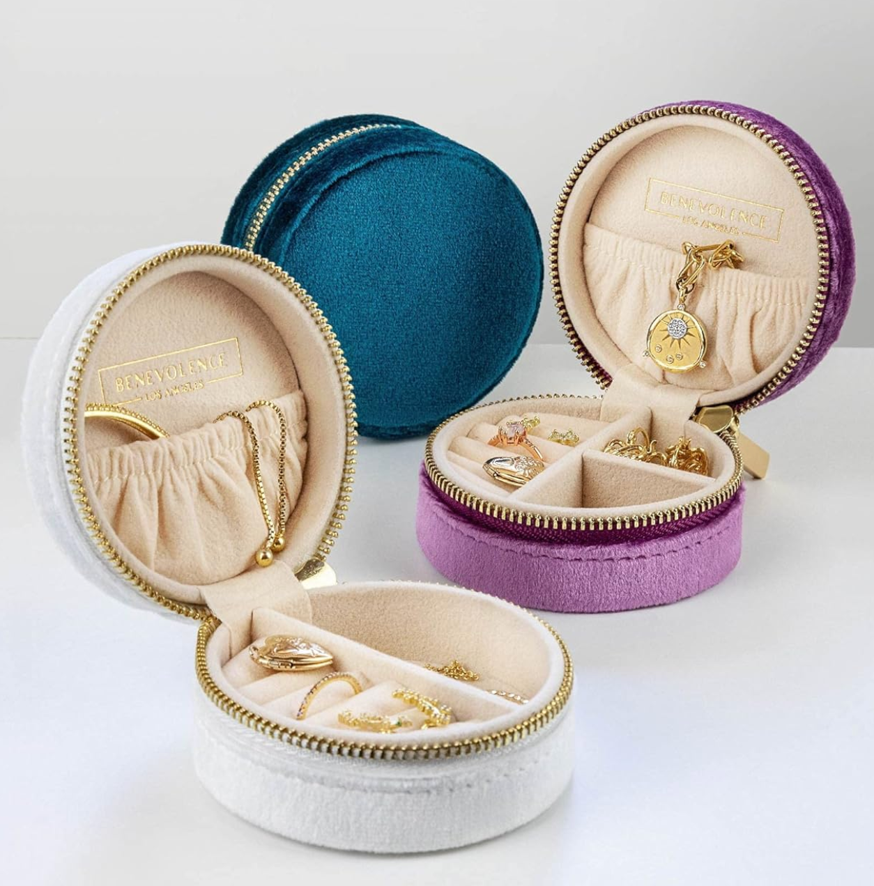 Three velvet question jewelry cases with golden zippers, successful teal, purple, and white, displaying golden necklaces and rings inside