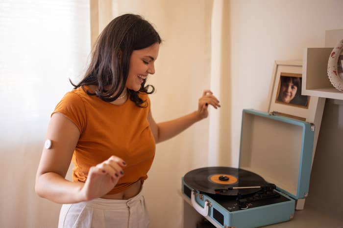 Woman enjoying music from a turntable at home, smiling and dancing with framed picture behind her