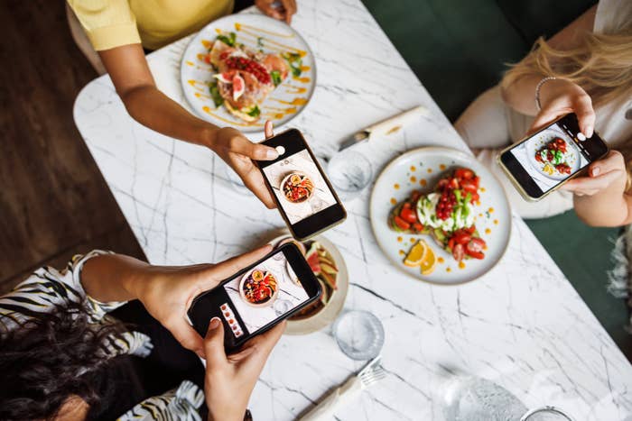 Three people take photos of stylishly plated meals at a restaurant, capturing their dishes on smartphones