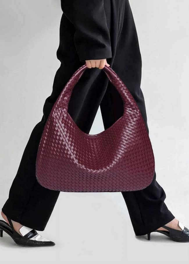 Person holding a ample woven handbag, styled with achromatic pants and achromatic heeled shoes, featured successful a buying article.