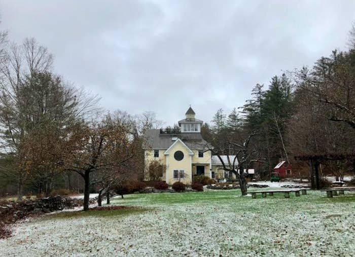 A large house with a turret is surrounded by a snowy lawn and trees, set against a cloudy sky