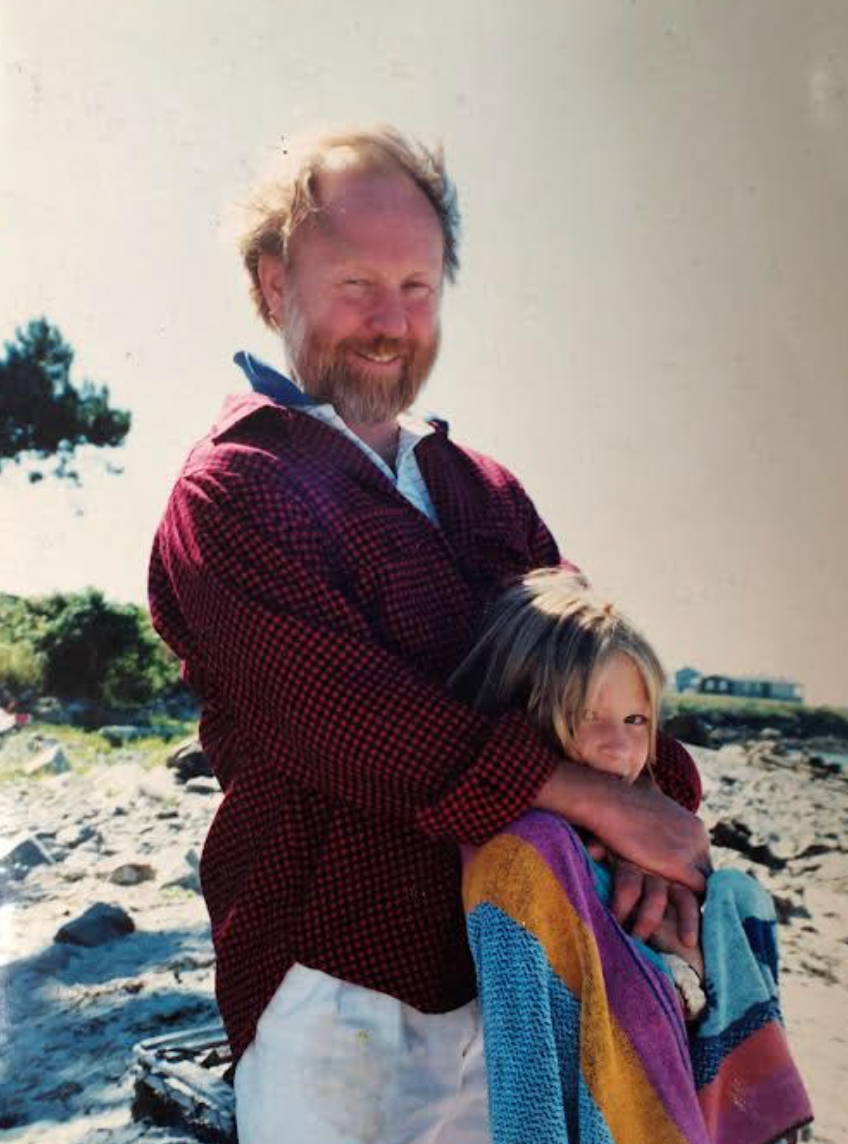 Man smiling and hugging a child wrapped in a towel on a rocky beach