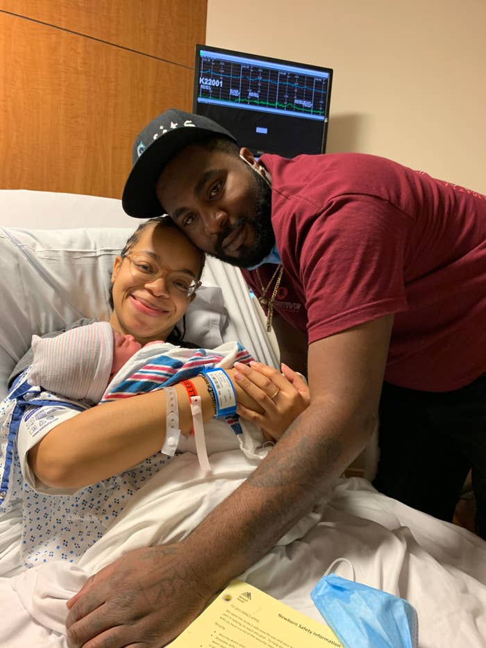 A joyful couple embraces their newborn baby in a hospital room, with medical equipment visible in the background