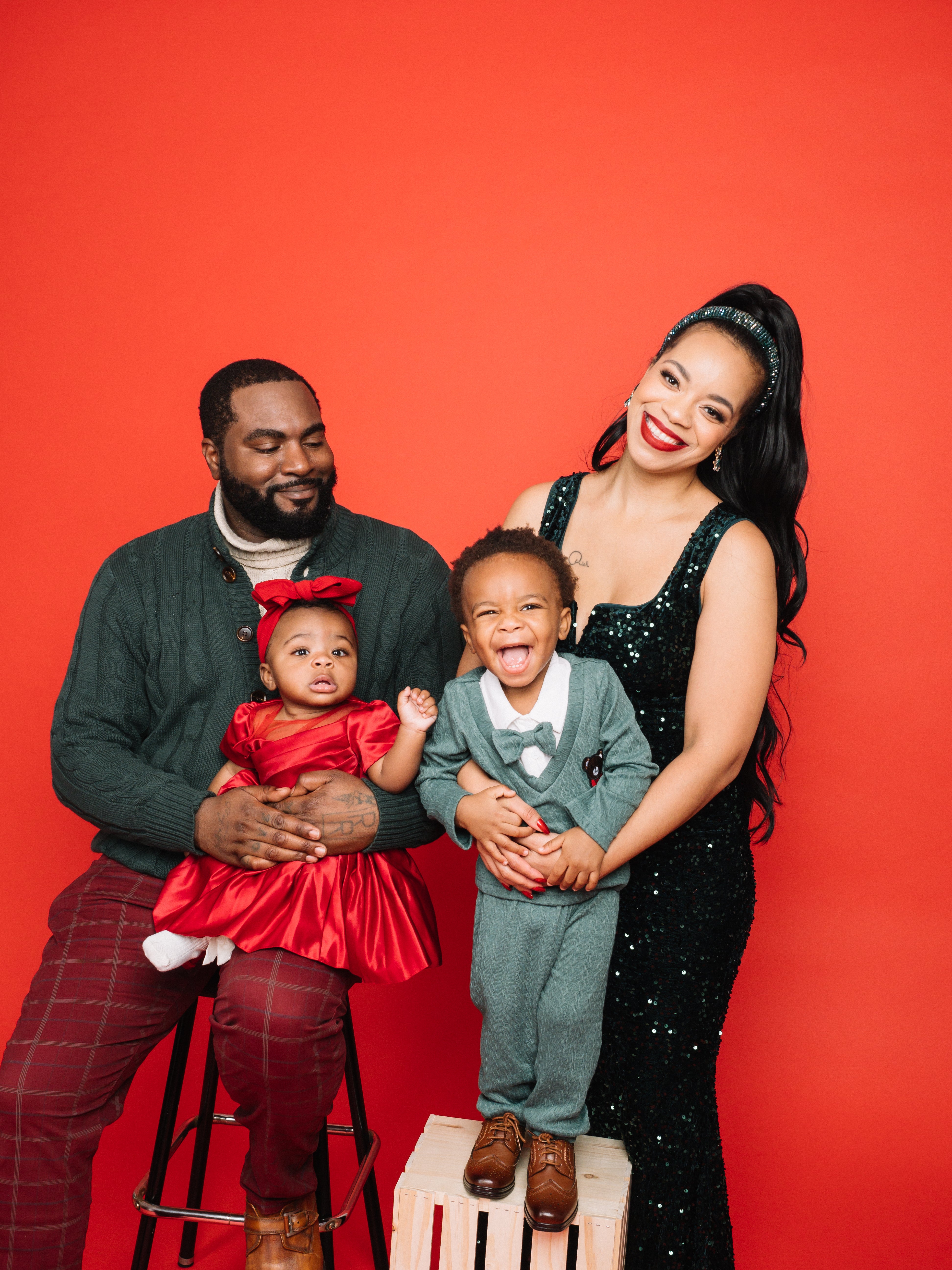Family poses in formal attire; woman in a sequin dress, man in sweater and plaid pants, children in a red dress and a suit with a bow tie