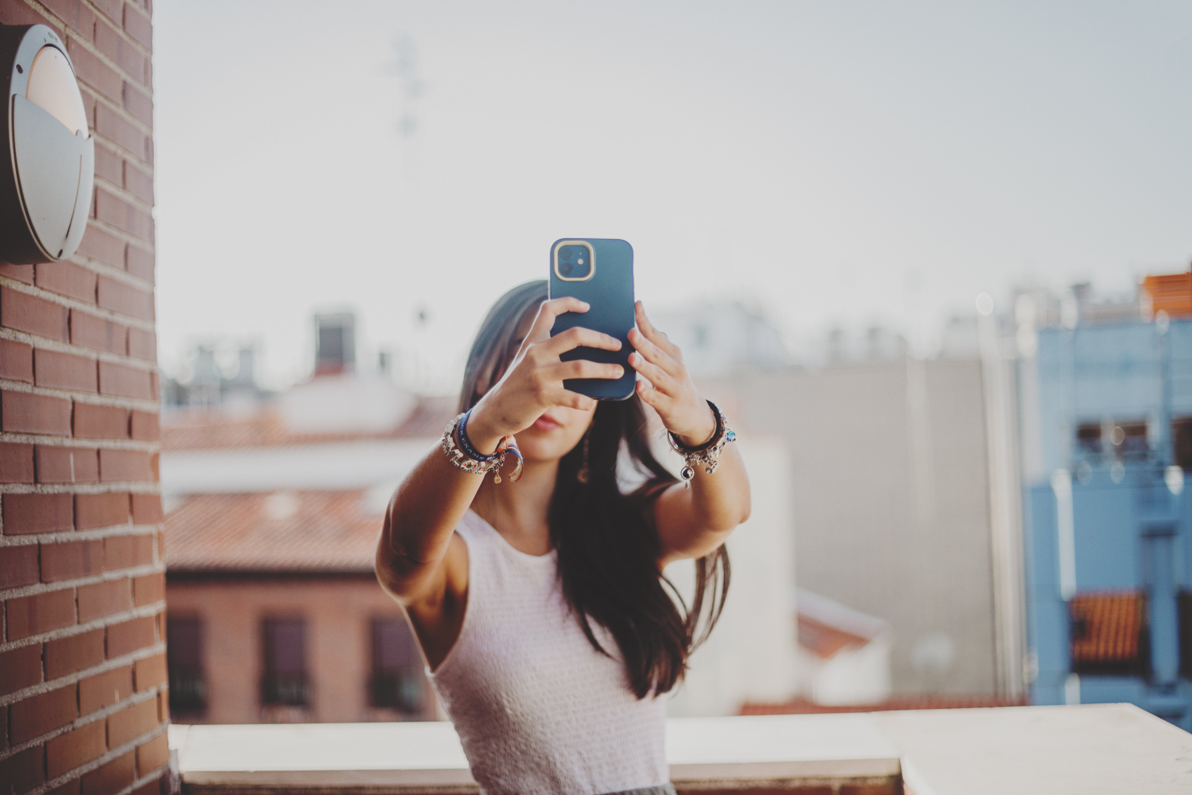 Person taking a selfie on a balcony with city rooftops in the background
