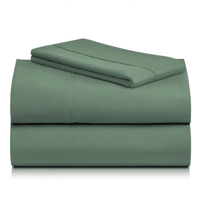 Stacked folded greenish  furniture  sheets and a pillowcase, suggesting luxury and comfortableness  for location  shopping
