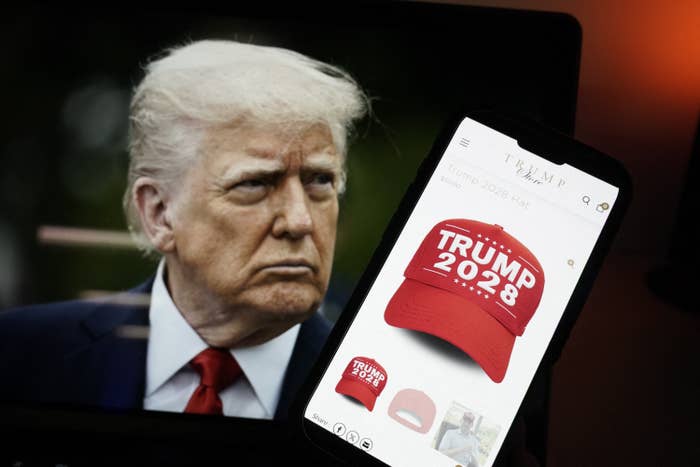 A smartphone displays an online listing for a &quot;Trump 2028&quot; hat next to a monitor showing a man's face