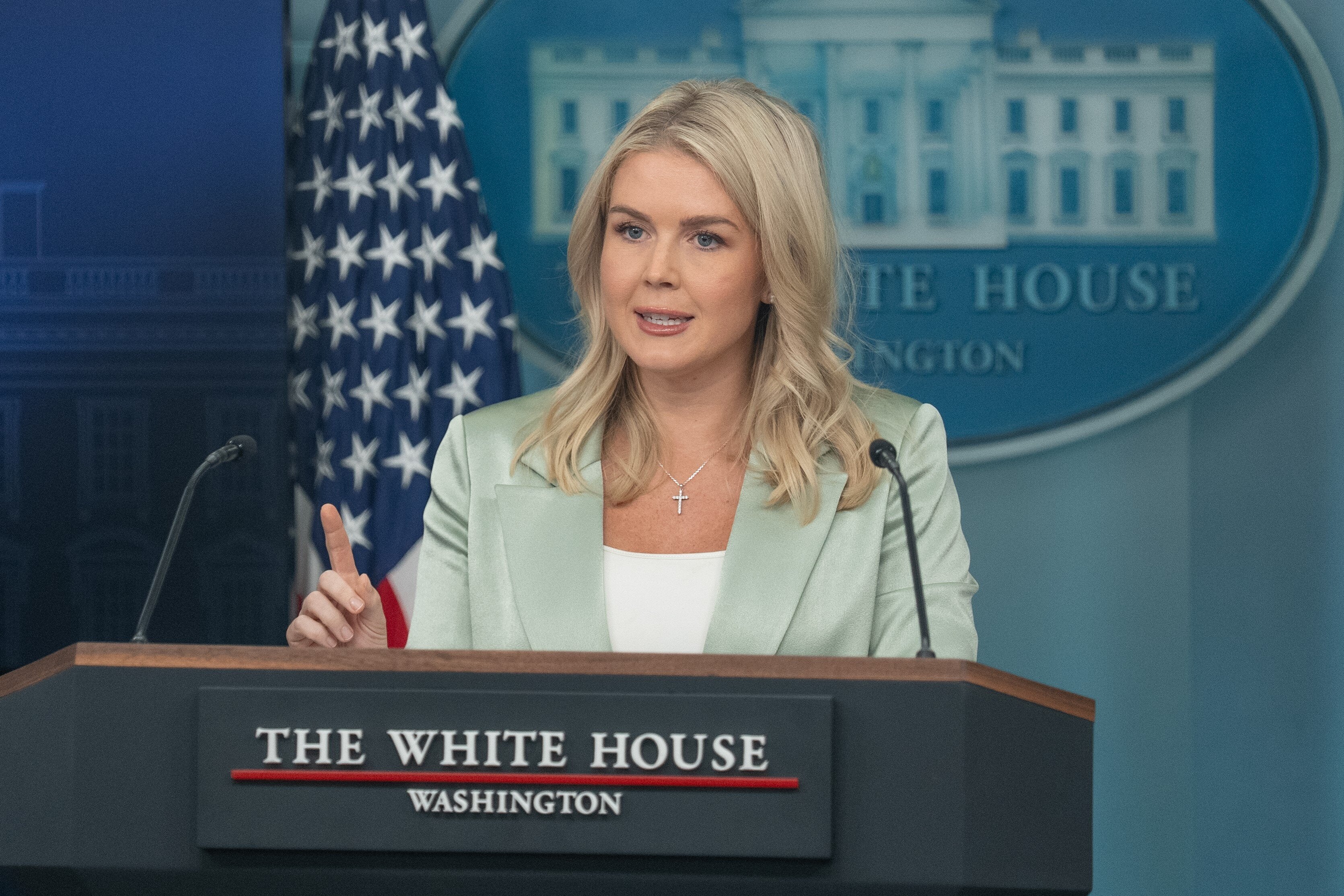 Person speaking at a White House podium during a press briefing, emphasizing a point with a raised finger