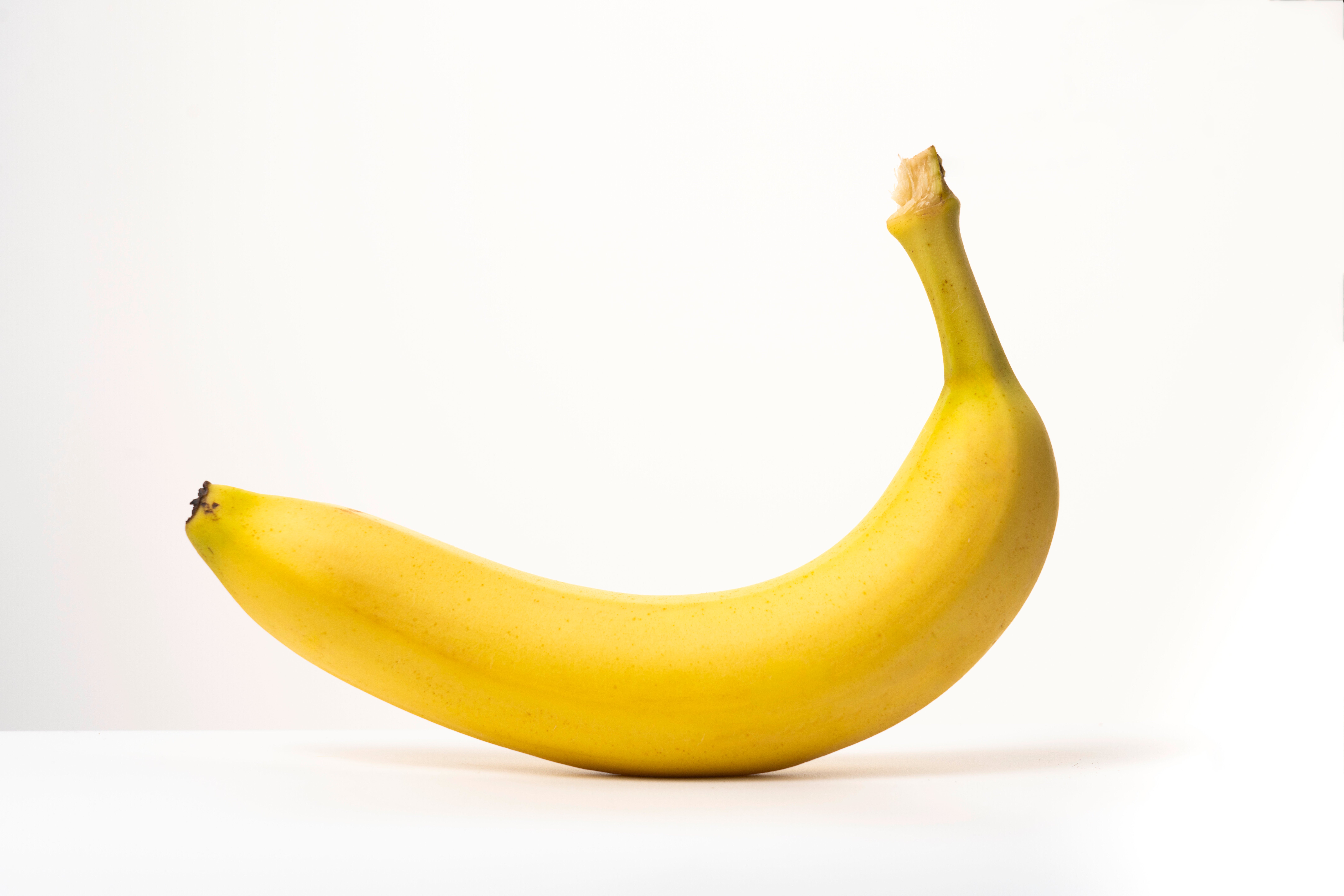 A ripe banana with a curved shape rests on a flat surface, isolated against a plain background