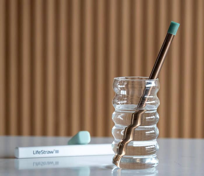 A reusable metallic  straw successful  a wavy solid  with a container  labeled "LifeStraw" connected  a table, showcasing eco-friendly beverage accessories