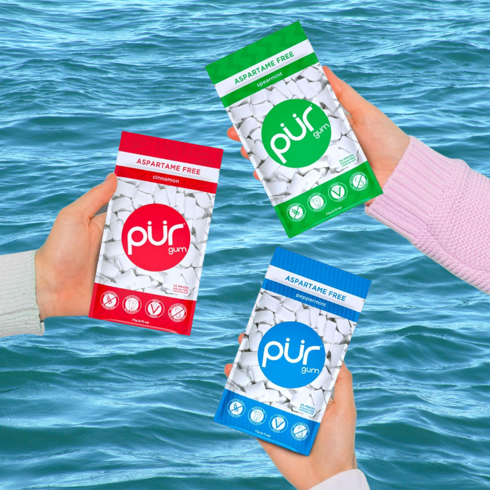 Three hands holding packs of aspartame-free chewing gum successful mint, spearmint, and cinnamon flavors, acceptable against a h2o background