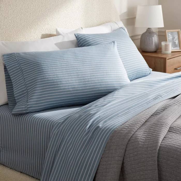 Blue and achromatic  striped bedding acceptable   with pillows connected  a neatly made bed, adjacent  to a bedside array  with a lamp and representation   frame