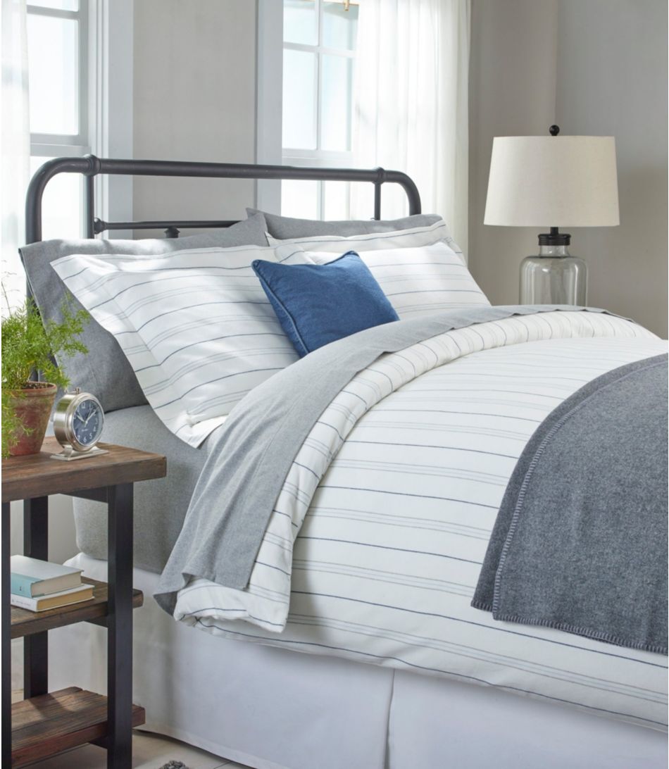 Cozy furniture  with striped bedding and a bluish  accent pillow, adjacent  to a woody  nightstand with a lamp and plant, successful  a bright, inviting room