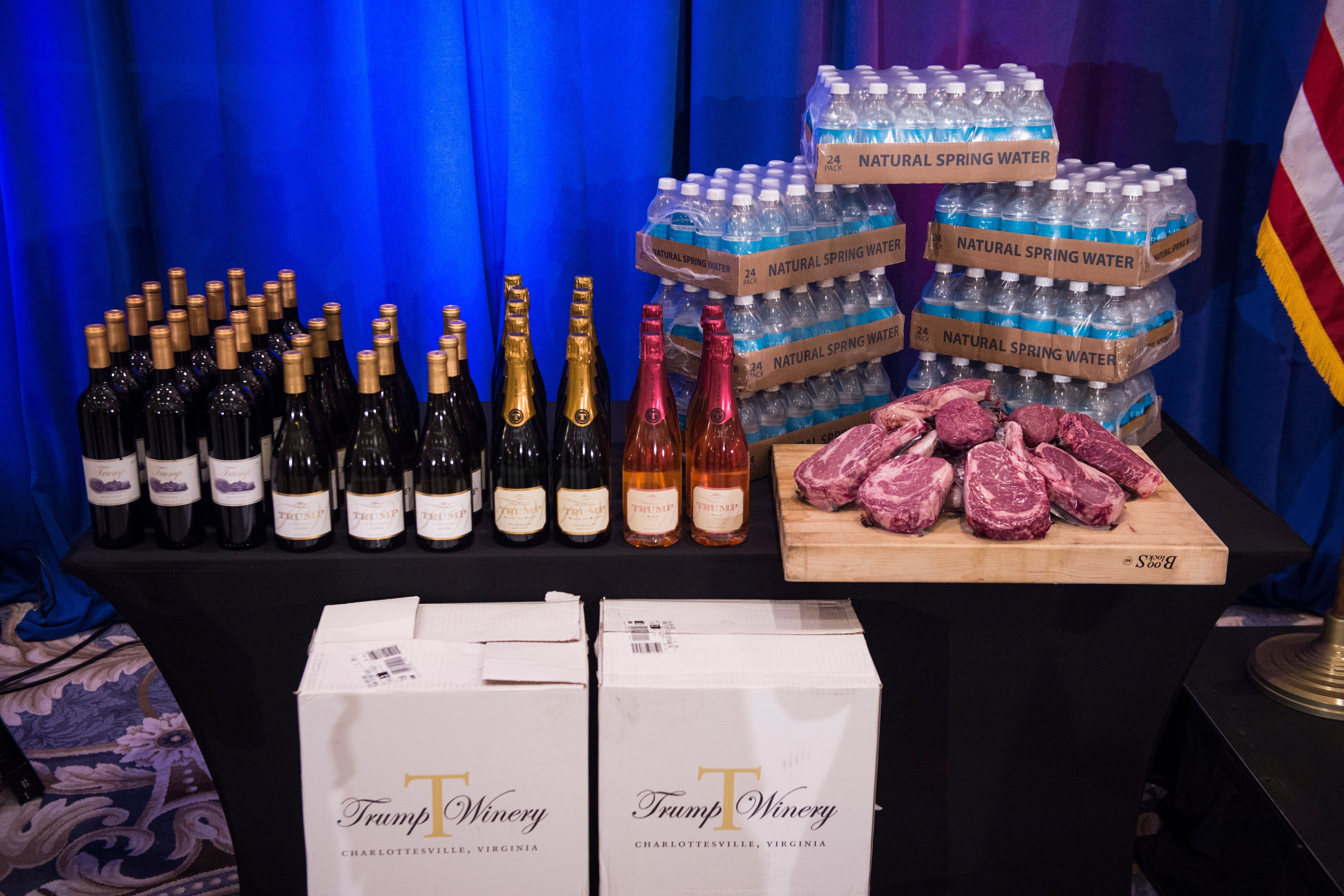 Table displaying wine bottles, water bottles, and raw steaks, with "Trump Winery" boxes beneath. The setup is arranged for a promotional display