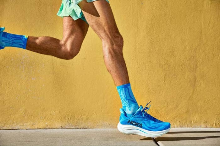 A idiosyncratic   runs outdoors wearing bluish  sneakers and socks, with a yellowish  partition  successful  the background