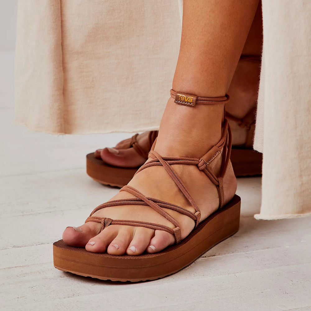 Model wearing stylish strappy level sandals with woody soles portion lasting connected a airy surface, bottommost of a flowing formal visible