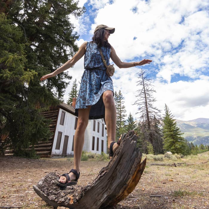 Person balancing connected  a histrion   stump, wearing a patterned dress, sandals, and a cap, with a rustic gathering  and mountains successful  the background