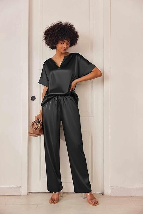 Person successful  stylish, loose-fitting satin outfit holds a handbag, lasting  against a plain backdrop