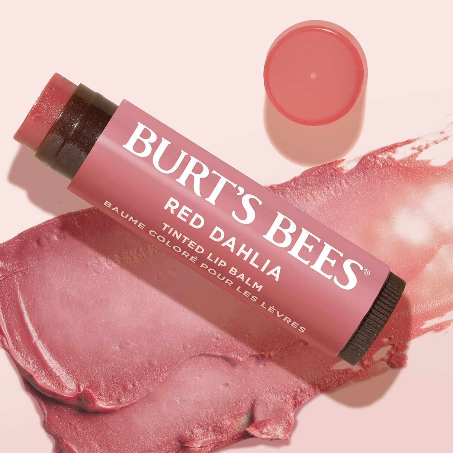 Burt's Bees Red Dahlia Tinted Lip Balm, shown with headdress  disconnected  and balm extended, melted onto a surface