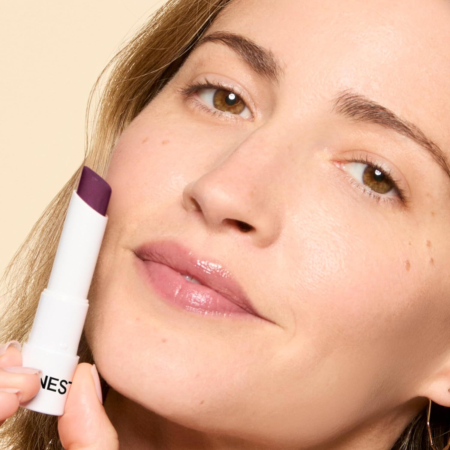 Person holding a lipstick adjacent   their lips, showcasing a neutral constitution  look