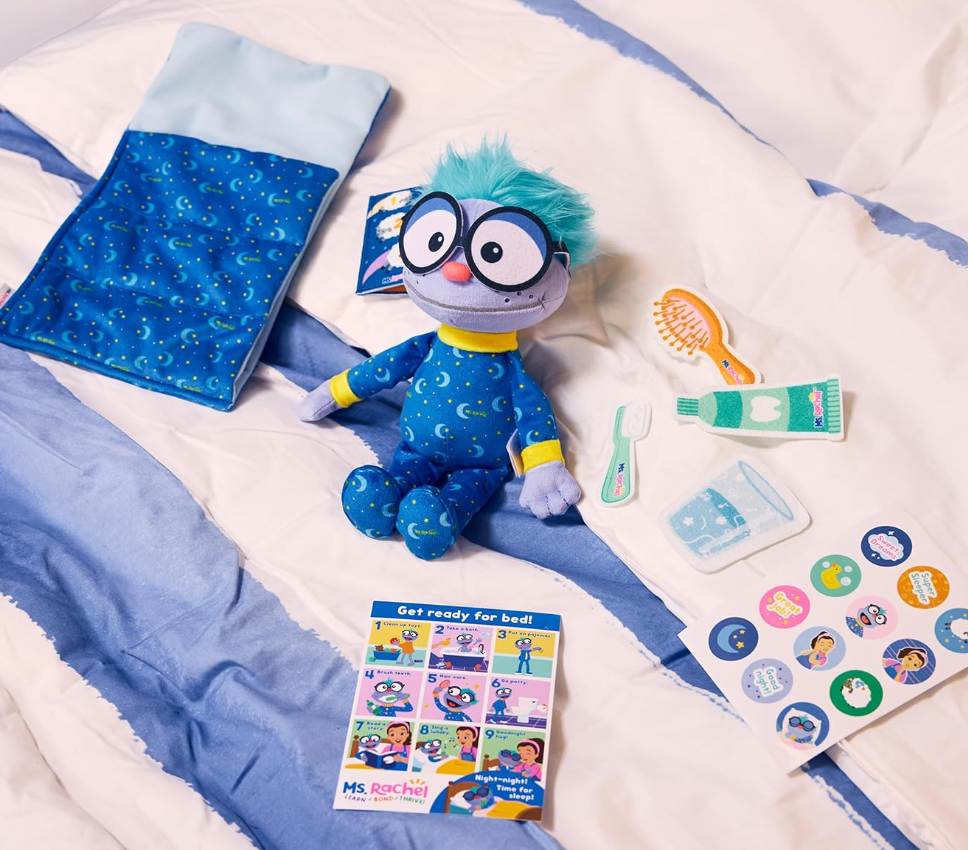 Plush artifact  with glasses, bluish  pajamas laid connected  a bed, surrounded by artifact  accessories similar  a toothbrush, toothpaste, and bedtime stickers