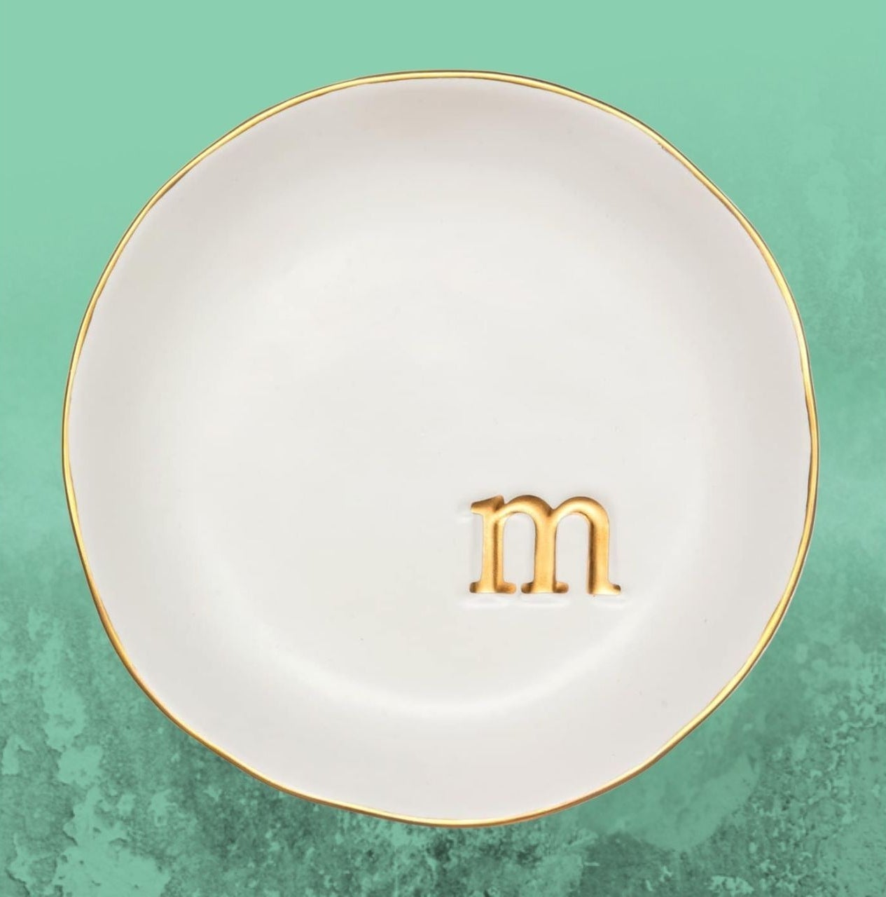Round crockery  with a golden  rim and the missive  "m" embossed successful  golden  astatine  the center, acceptable   against a textured background