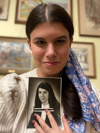 Person holding a vintage photo of a woman, both with similar hairstyles and attire, creating a reflective comparison across generations