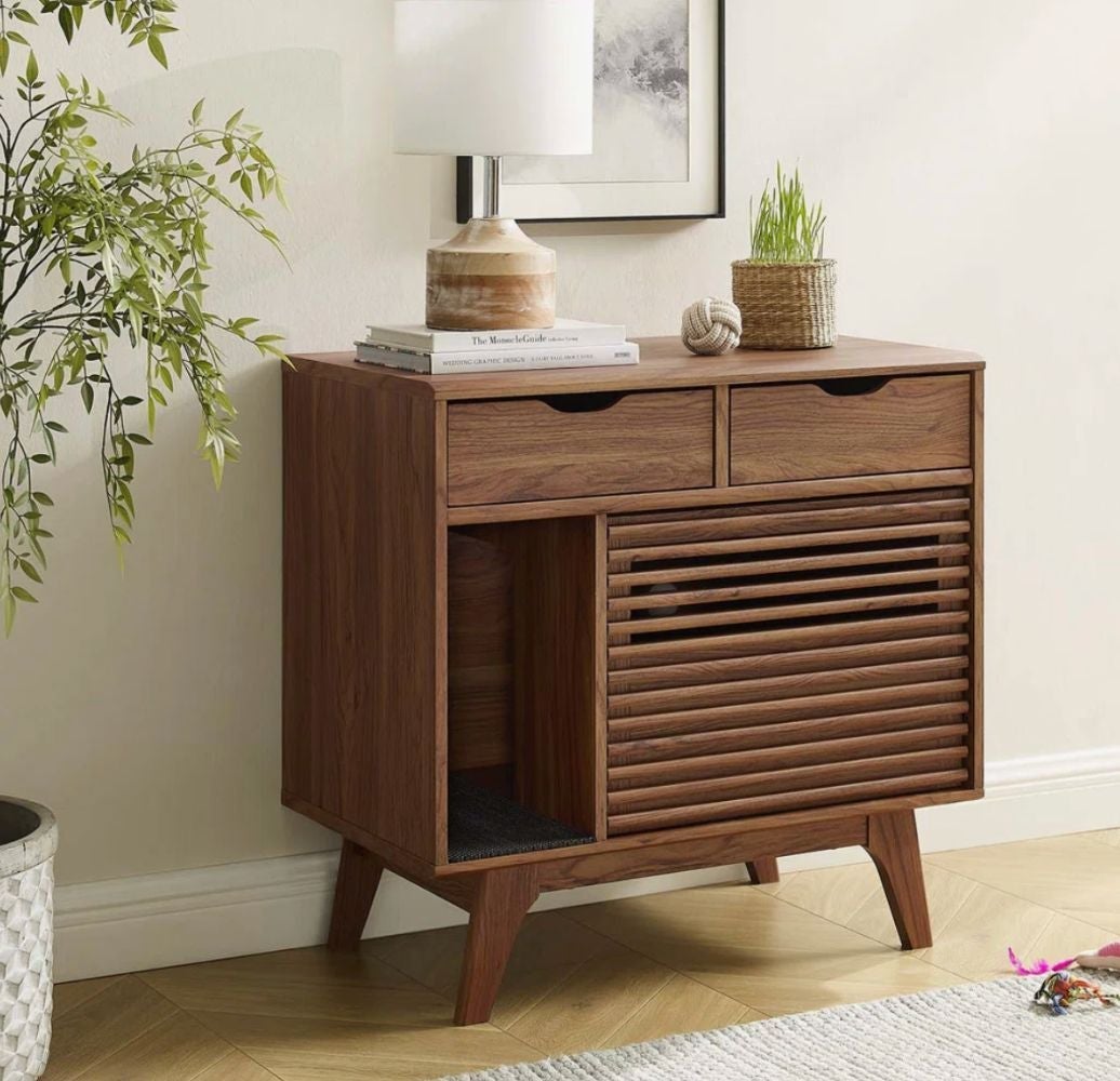 A modern wooden side table with two drawers, slatted door, potted plant, and lamp on top, placed in a stylish room setting