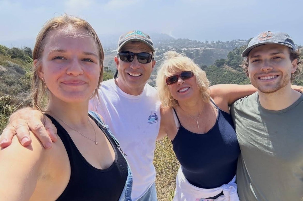 Four people smiling while outdoors on a scenic hike, with hills and cloudy skies in the background