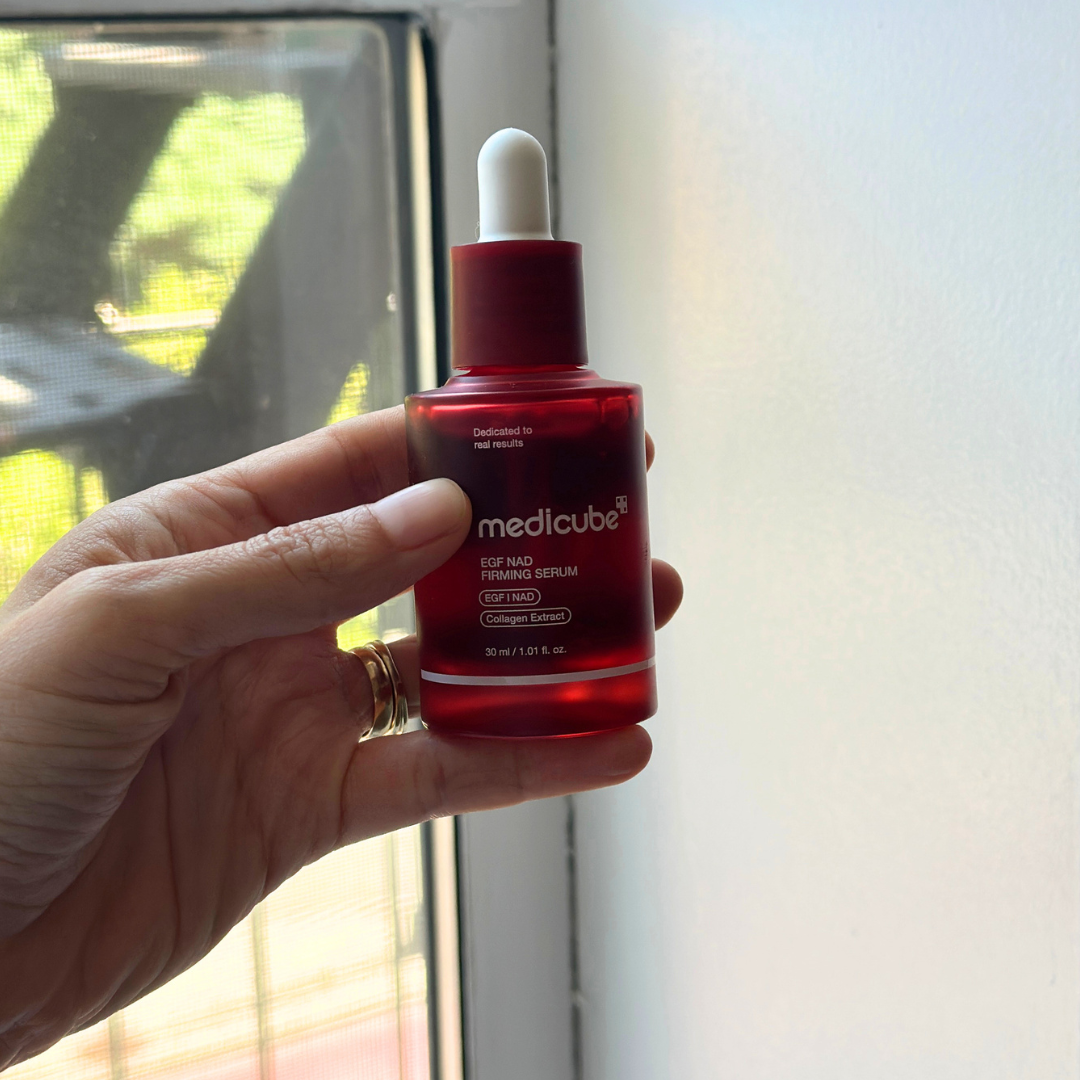 A manus  holds a vessel  of Medicube EGF NAD Firming Serum by a window