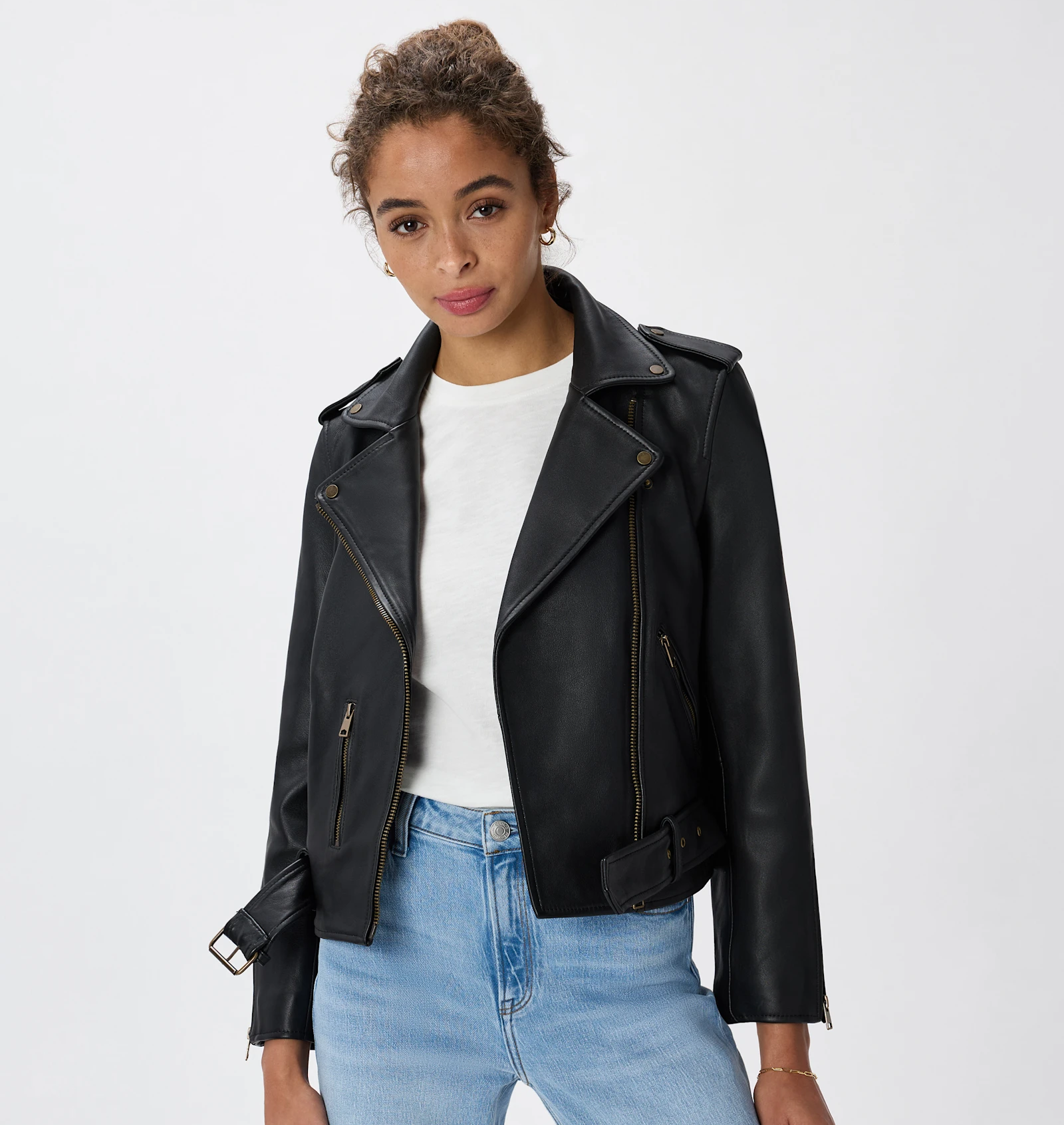 Person wearing a casual biker-style leather overgarment implicit a achromatic garment and airy denim jeans, posing for a manner article