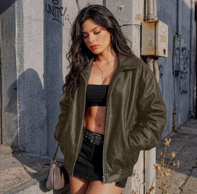 Woman successful stylish achromatic harvest top, skirt, and leather overgarment leans against a wall. She is outdoors; the mounting has an municipality feel