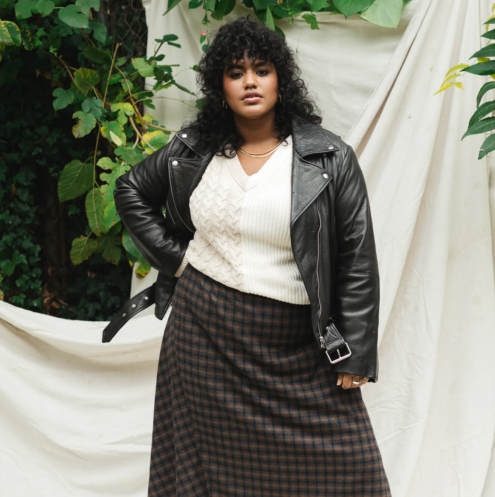Person successful a leather jacket, achromatic sweater, and plaid skirt poses confidently against a earthy backdrop