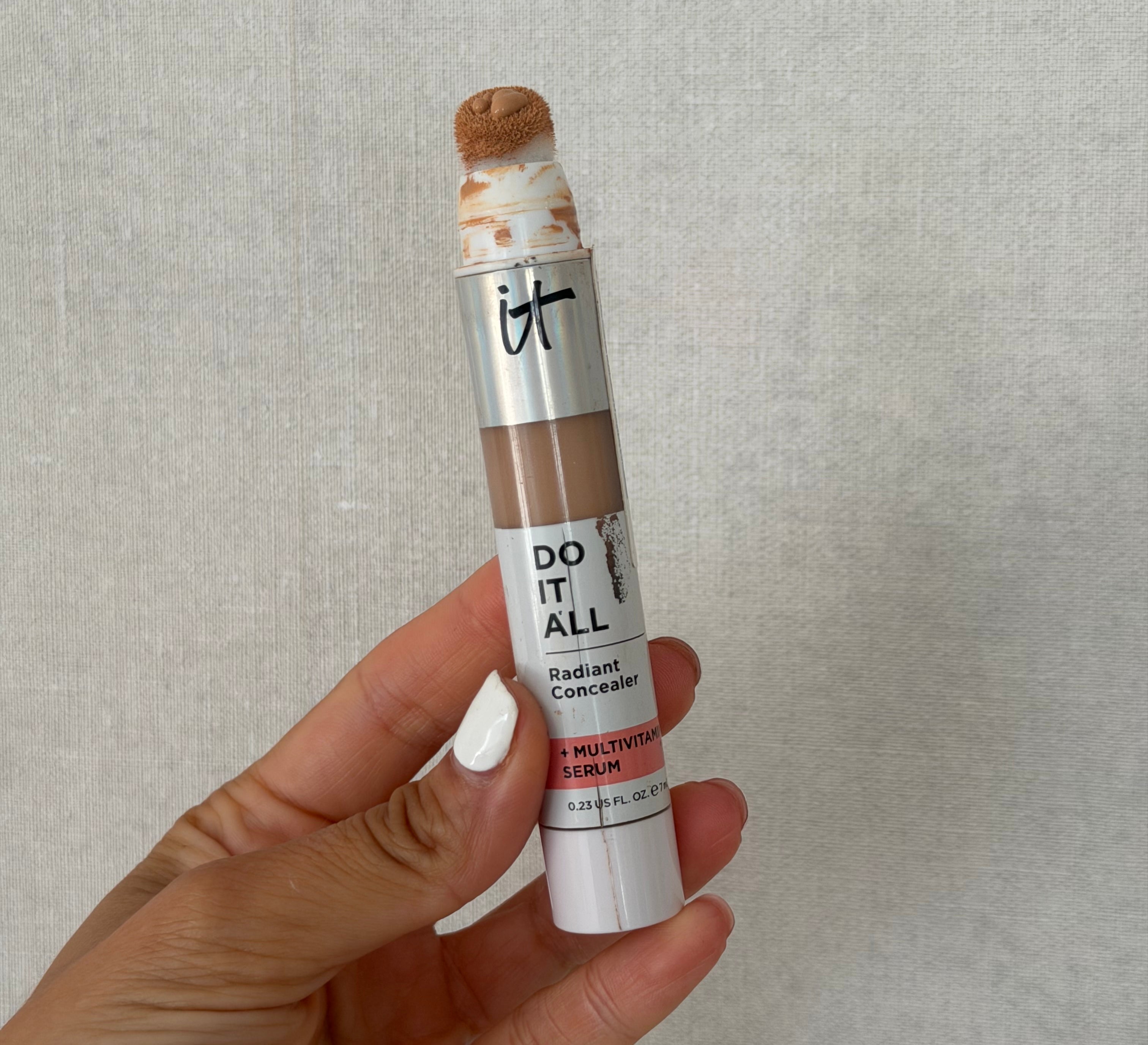 Hand holding a conduit  of IT Cosmetics Do It All Radiant Concealer with Multivitamin Serum