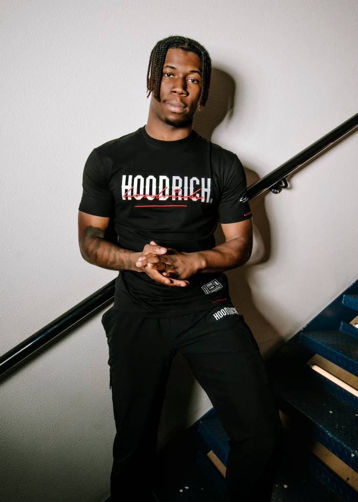 Young 6ix wears Hoodrich, standing on a staircase.