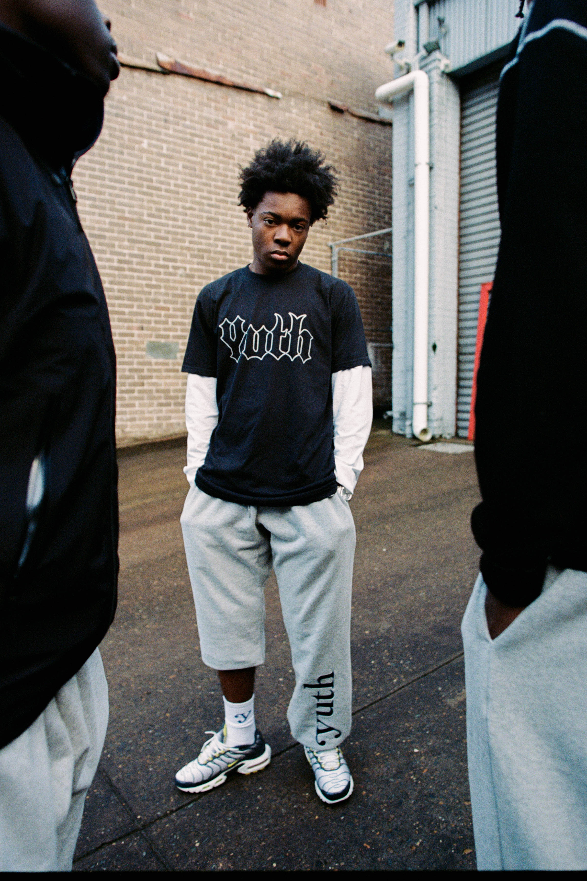 A young man wears a youth t-shirt and track pants