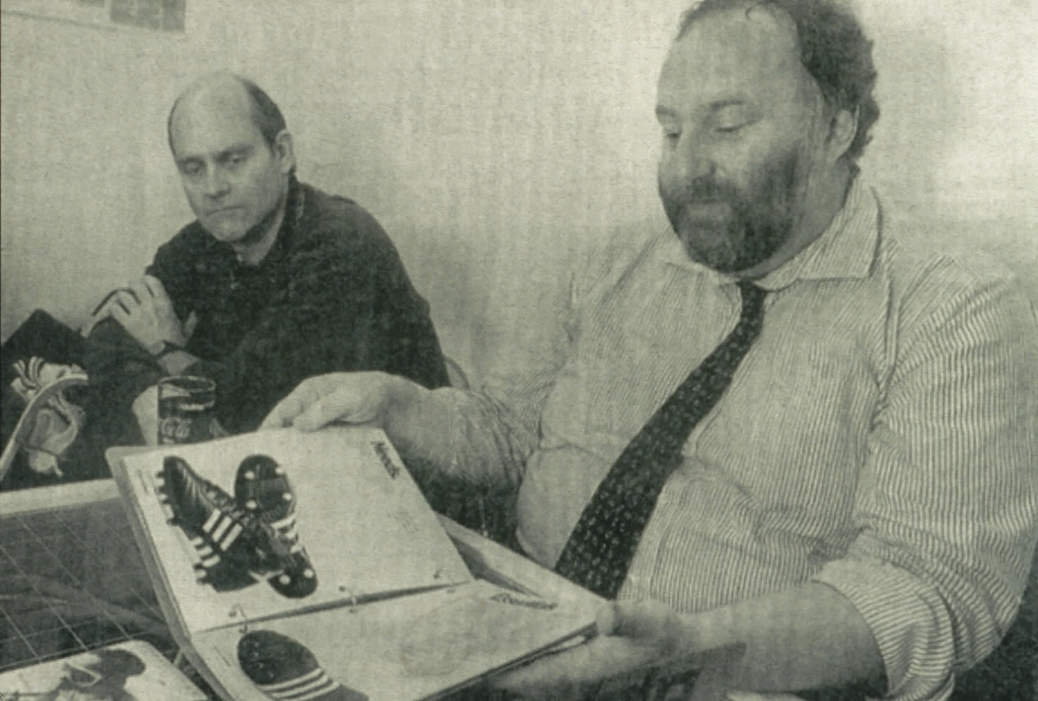 Peter Moore and Rob Strasser, Strasser showing a catalog of Adidas cleats