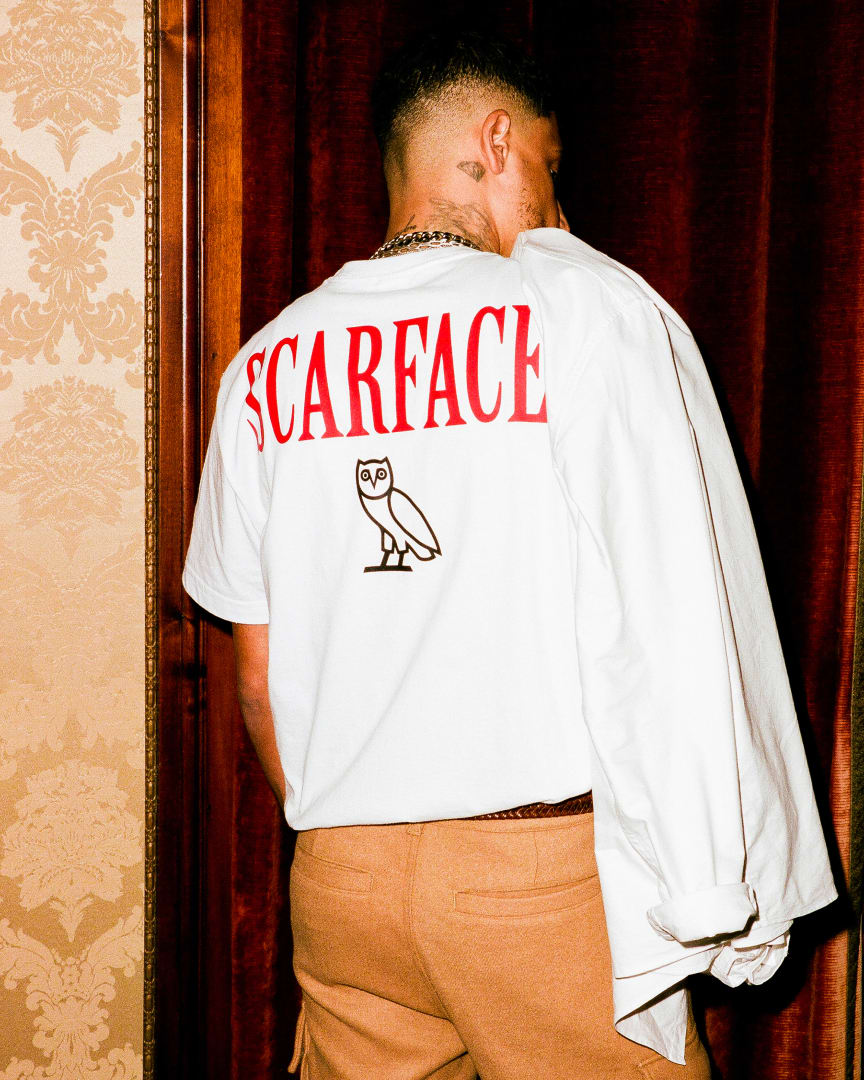 Model wearing a white T-shirt with red lettering that reads &quot;SCARFACE&quot;, with the OVO owl underneath the text