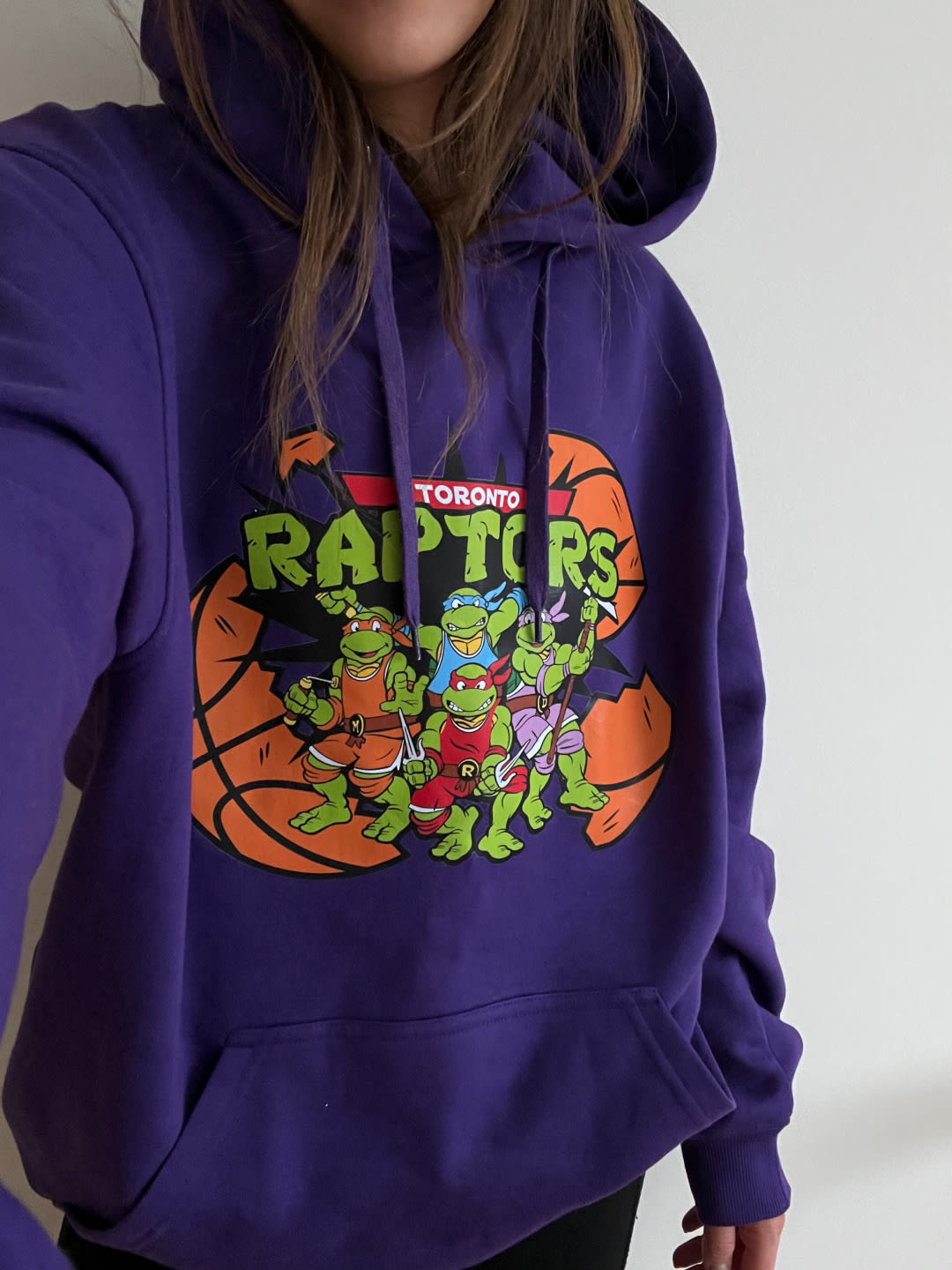 A model wearing a purple hoodie that reads &quot;Toronto Raptors&quot; with the Teenage Mutant Ninja Turtles on it