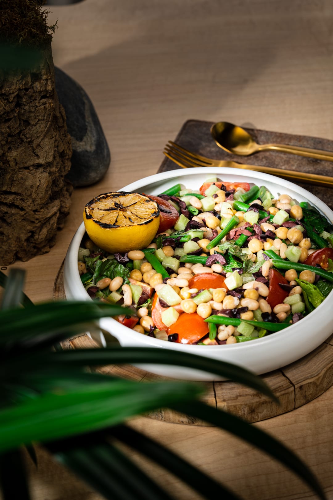 A bowl of beans and veggies with a roasted lemon.