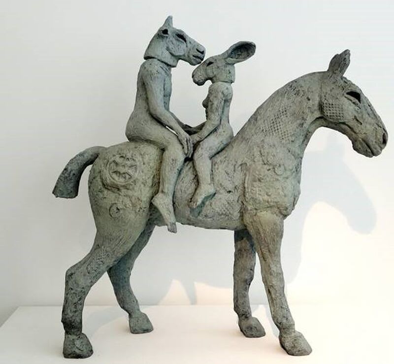 A sculpture of two animal-faced humans riding a horse.
